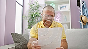 Handsome middle-aged caucasian man enjoy reading a smart document, expressing positive joy while sitting confidently on the sofa