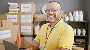 Handsome middle-aged caucasian man exudes confidence, smiles while volunteering at community charity center, adeptly using laptop