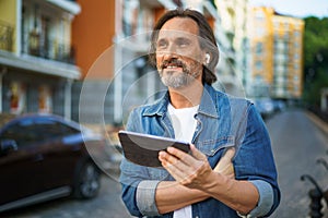 Handsome middle aged freelancer man using tablet having a call while walking on urban streets. Mature man use wireless