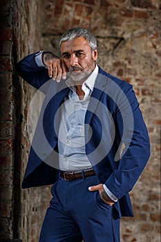 A handsome middle-aged man in a blue formal suit poses on a gray background. Portrait of a businessman. A handsome middle-aged man