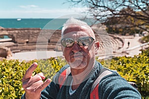 handsome middle aged man visiting tarraco archaeological complex, Tarragona - Happy tourist taking a selfie in front of roman photo