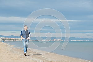 Handsome middle-aged man walking at the beach. Attractive happy smiling mid adult male model posing at seaside in blue jeans, t-