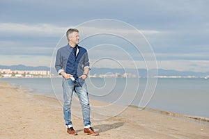 Handsome middle-aged man walking at the beach. Attractive happy smiling mid adult male model posing at seaside in blue jeans, t-