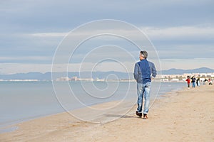 Handsome middle-aged man walking at the beach, back view.  Full-length outdoor portrait of beautiful man