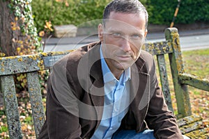 Handsome middle aged man wearing shirt and jacket sitting on park bench