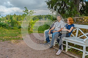 Handsome middle-aged man and young pretty lady sitting on bench