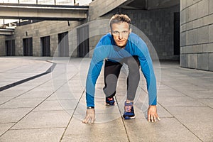 Handsome middle aged serious man in blue black sports uniform and headphones and fitness tracker is running in the city.