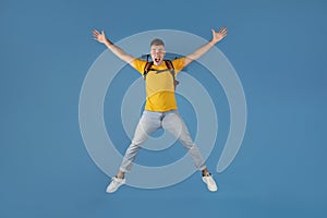 Handsome millennial guy with backpack jumping in excitement over blue studio background