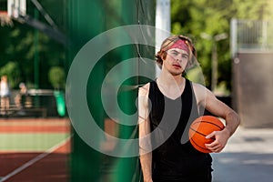 Handsome millennial player in sportswear ready to play ball at outdoor basketball court, empty space