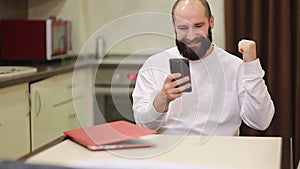 Handsome millennial single guy sit at table in kitchen hold smart phone