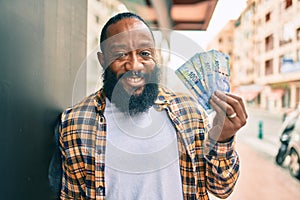 Handsome modern african american man with beard smiling positive standing at the street showing 100 south african rands banknotes