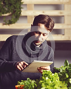 Handsome modern grower using his tablet while growing plants ind