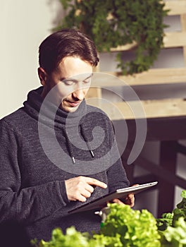 Handsome modern grower using his tablet while growing plants ind