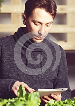 Handsome modern grower using his tablet while growing plants ind