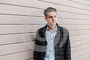 Handsome modern young man with a hairstyle in a gray checkered jacket in a stylish shirt in jeans is standing