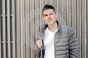 Handsome modern young man with a stylish hairstyle in a fashionable gray jacket in a trendy white T-shirt poses