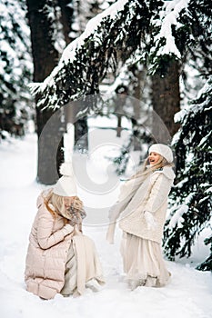 Handsome mother and daughter are having fun outdoor in winter time. Playing with snow in forest between snowy trees