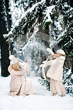 Handsome mother and daughter are having fun outdoor in winter time. Playing with snow in forest between snowy trees