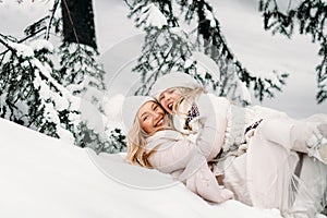 Handsome mother and daughter are having fun outdoor in winter time. Playing with snow in forest between snowy trees