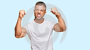 Handsome muscle man wearing casual white tshirt angry and mad raising fists frustrated and furious while shouting with anger