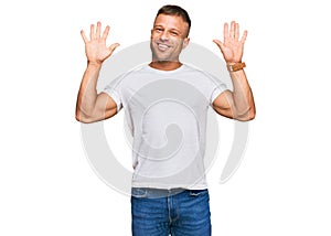 Handsome muscle man wearing casual white tshirt showing and pointing up with fingers number ten while smiling confident and happy