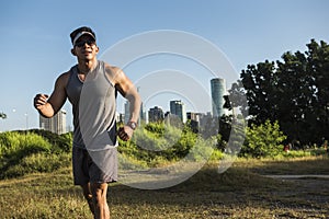 A handsome and muscular asian man jogs through a grassy field near the city skyline. Cardiovascular training