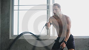 handsome Muscular bodybuilder man exercises with battle ropes at gym . Shirtless fitness young sport man training .work out