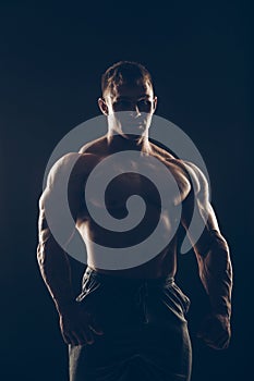 Handsome muscular bodybuilder posing over black