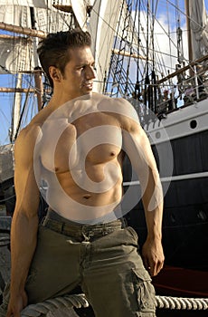 Handsome muscular captain poses by his sailboat with all the sails drawn.