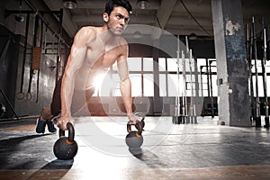 Handsome muscular man doing pushup exercise with dumbbell in a crossfit workout.