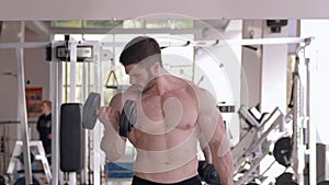 Handsome muscular man doing sports strength exercise with dumbbells in hands during training in gym