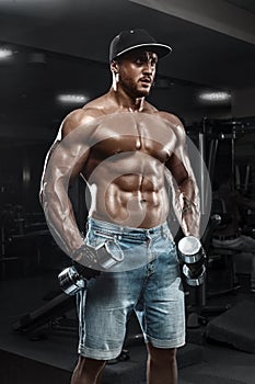 Handsome muscular man with dumbbells working out in gym, doing exercise