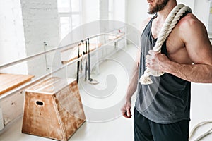 Handsome muscular man holding on shoulder rope workout in light gym