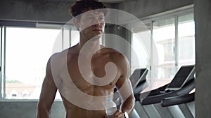 Handsome muscular man running on treadmill finished exercise drinking water in fitness gym . Shirtless sport guy workout on