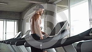 Handsome muscular man running on treadmill finished exercise and wiping sweat with towel in fitness gym . Shirtless sport guy