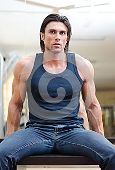 Handsome, muscular man sitting on desk indoors