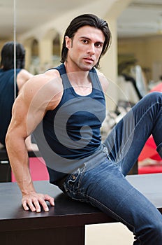 Handsome, muscular man sitting on desk, with jeans and tanktop