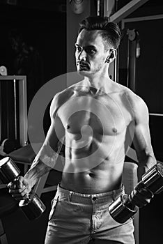 Handsome muscular man working out with dumbbells at gym. Bodybuilding, sport and fitness lifestyle. Black and white
