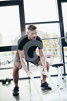 handsome muscular sportsman working out with ropes photo