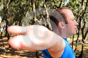 Handsome muscular young man is doing stretching exercises in forest. Sportsman wearing sportswear in landscape nature outdoor.