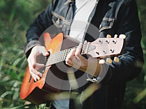 Handsome musician playing acoustic guitar at the grass field blur background. World music day. music and instrument concept