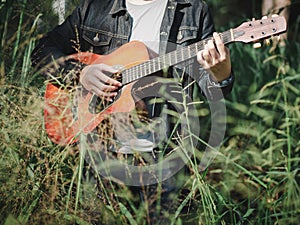 Handsome musician playing acoustic guitar at the grass field blur background. World music day. music and instrument concept