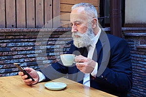 Handsome old man drinking coffee while surfing in mobile phone