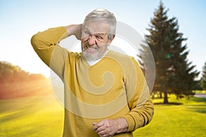 Handsome old man touching back of neck in pain.