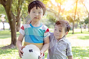 Handsome older brother holding ball and ready for playing in the park with younger brother. Little boy is always accompanied with