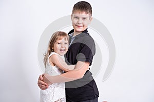 Handsome older brother teenager hugging his cute little sister on white background