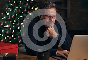 Handsome older man using laptop computer, shopping online. Christmas tree in the background