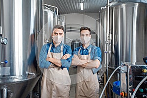 Handsome owners of brewery in masks and aprons, near brewing kettles