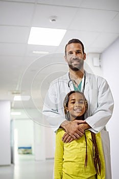 Pediatrician doctor smiling with his little girl patient at hospital