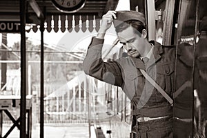 Handsome pensive male British soldier in WW2 vintage uniform at train station standing on train, putting on hat